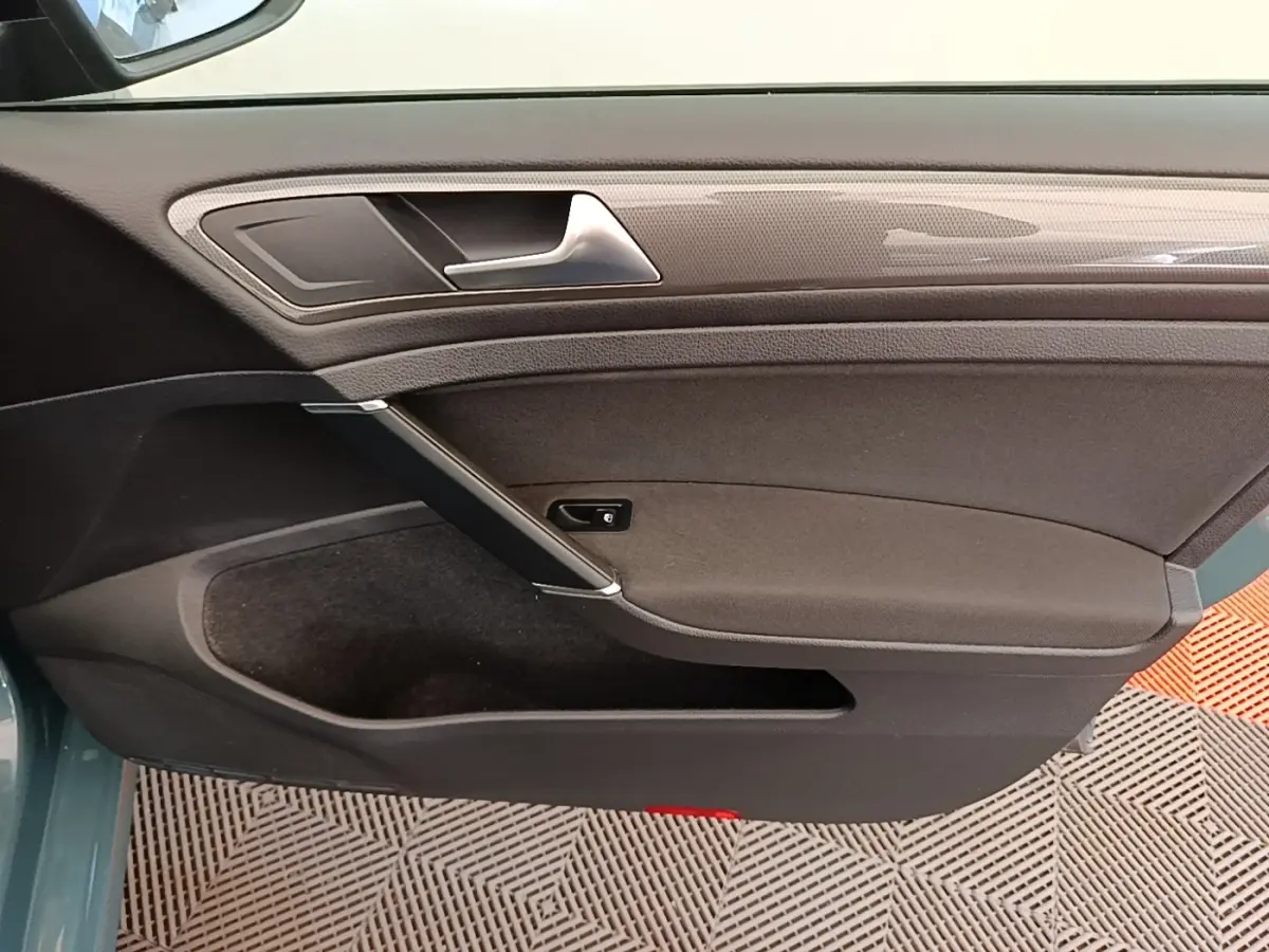 Vue rapprochée de la porte intérieure côté gauche d’une Volkswagen Golf 1.0 TSI 115 BVM6 IQ.DRIVE avec garniture noire et insert décoratif gris.
