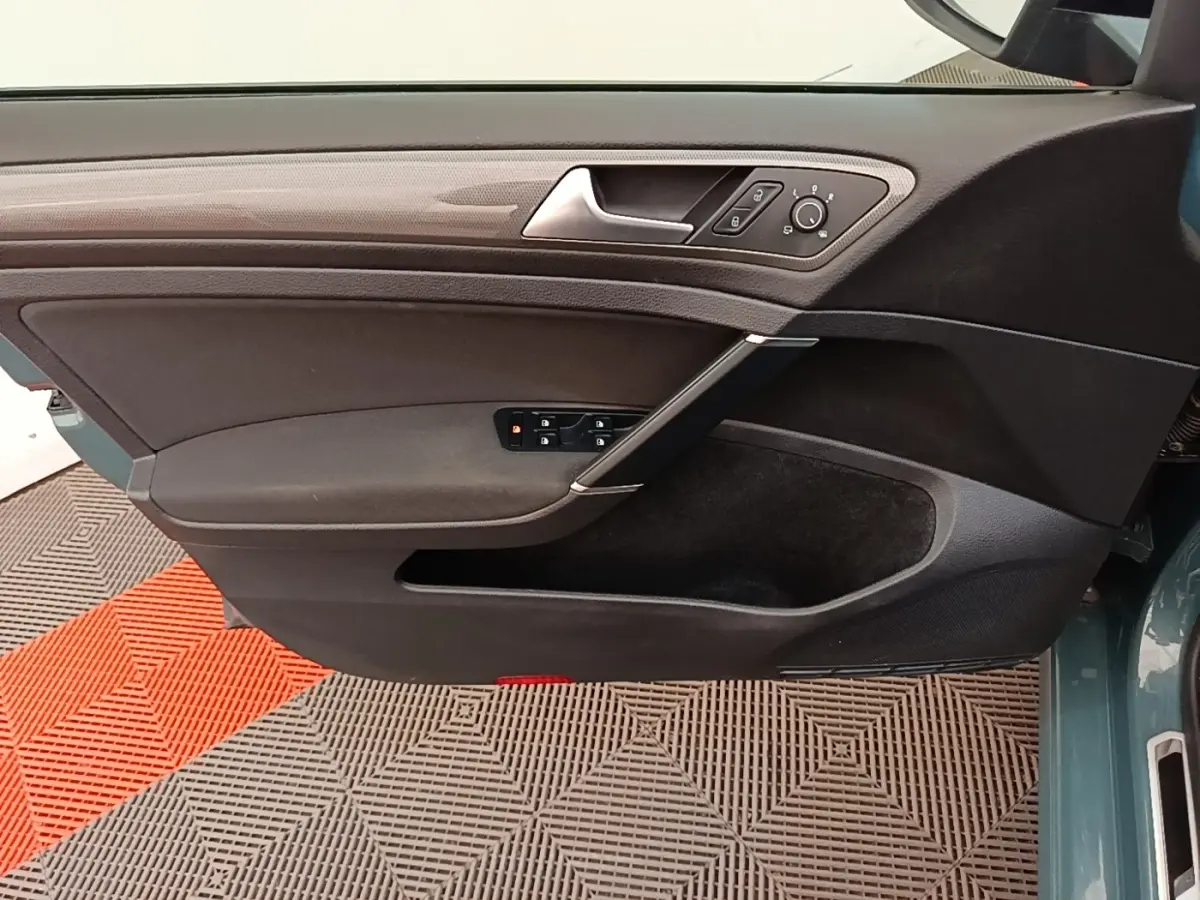 Vue intérieure côté gauche de la porte avant d’une Volkswagen Golf bleu, avec commandes électriques et poignée argentée.