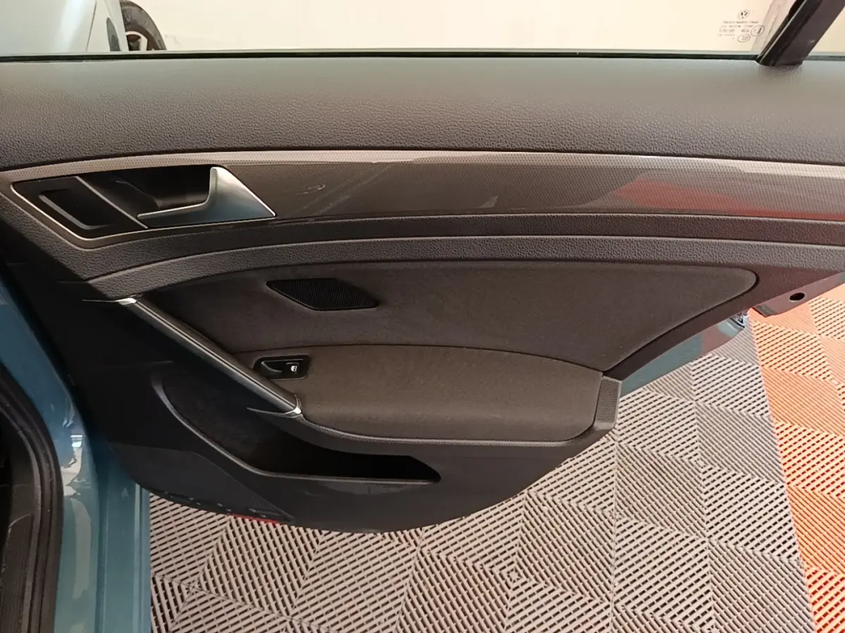 Vue intérieure côté gauche de la porte avant d’une Volkswagen Golf bleu 2020 avec garniture noire et poignée argentée.
