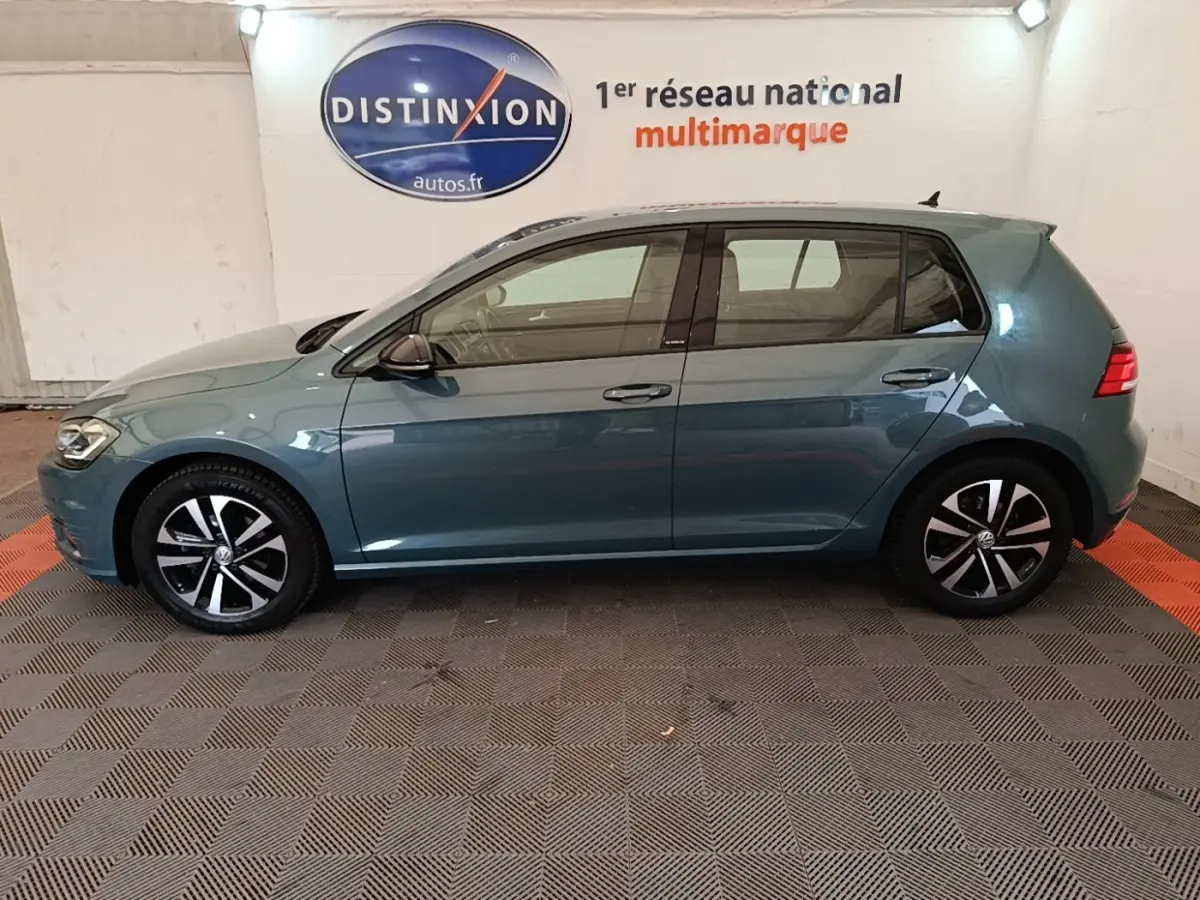 Profil latéral gauche d'une Volkswagen Golf bleu 2020 avec jantes alliage et vitres teintées en intérieur showroom.