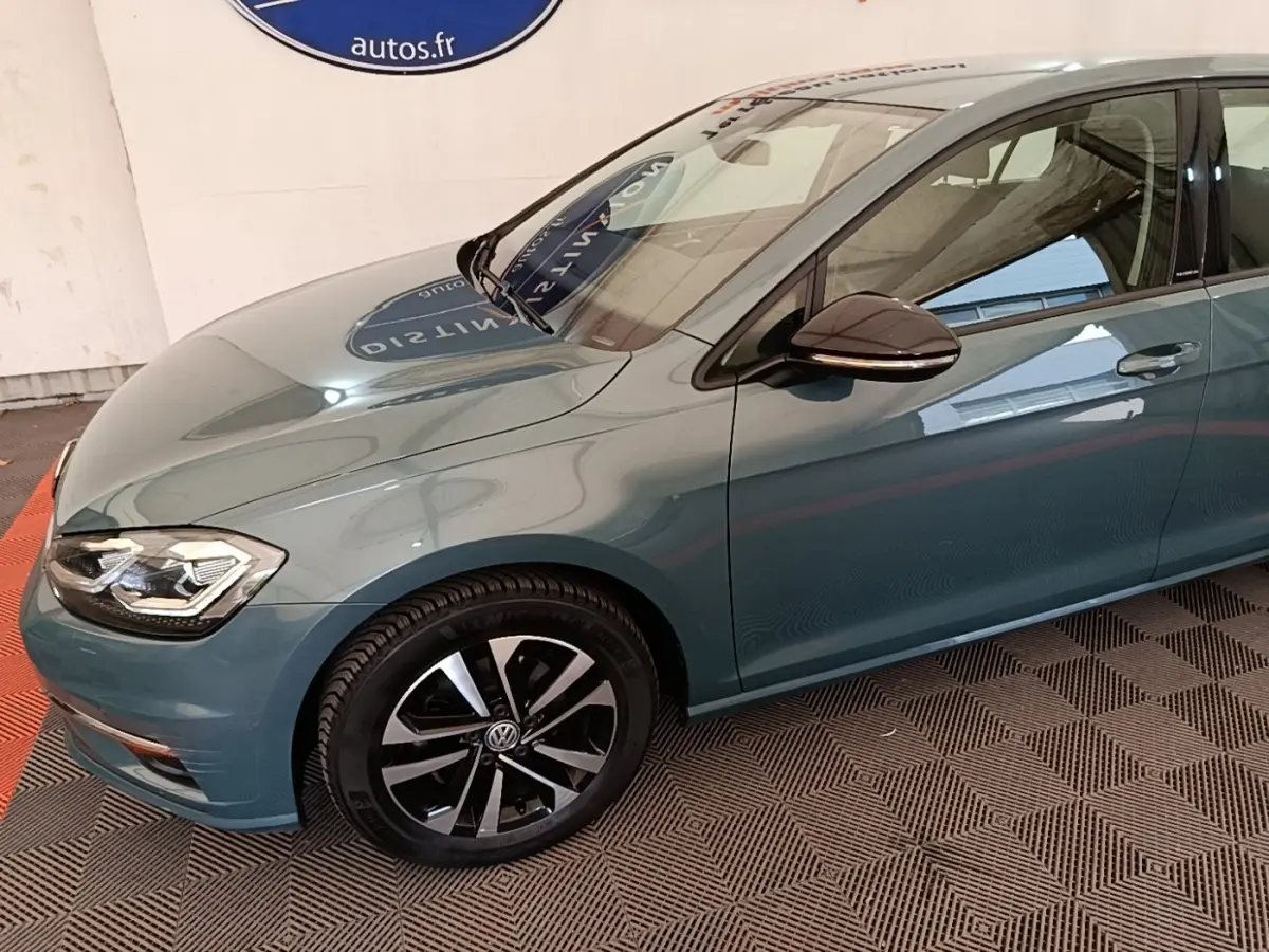 Vue 3/4 avant droit d’une Volkswagen Golf bleu métallisé avec jantes alliage noires et rétroviseur ton caisse.