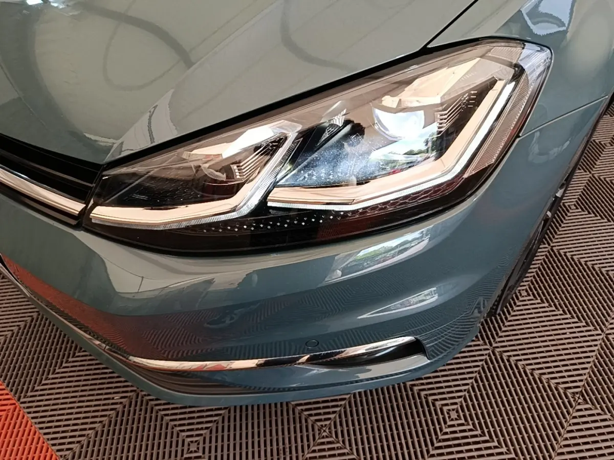 Gros plan sur le phare avant droit d’une Volkswagen Golf bleu 2020 avec détails LED et pare-chocs chromé.