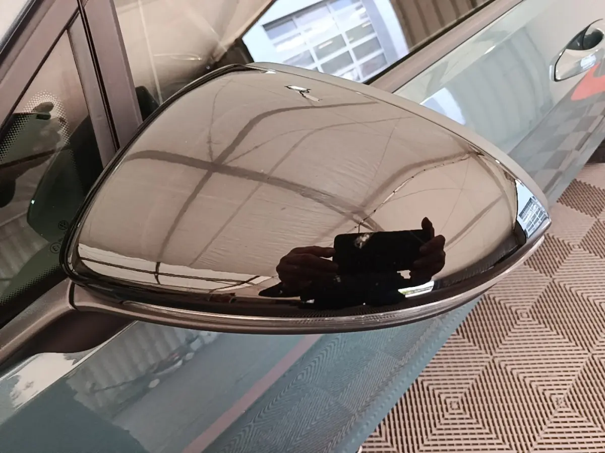 Rétroviseur droit chromé d'une Volkswagen Golf bleu, vue rapprochée avec reflet du plafond et main.