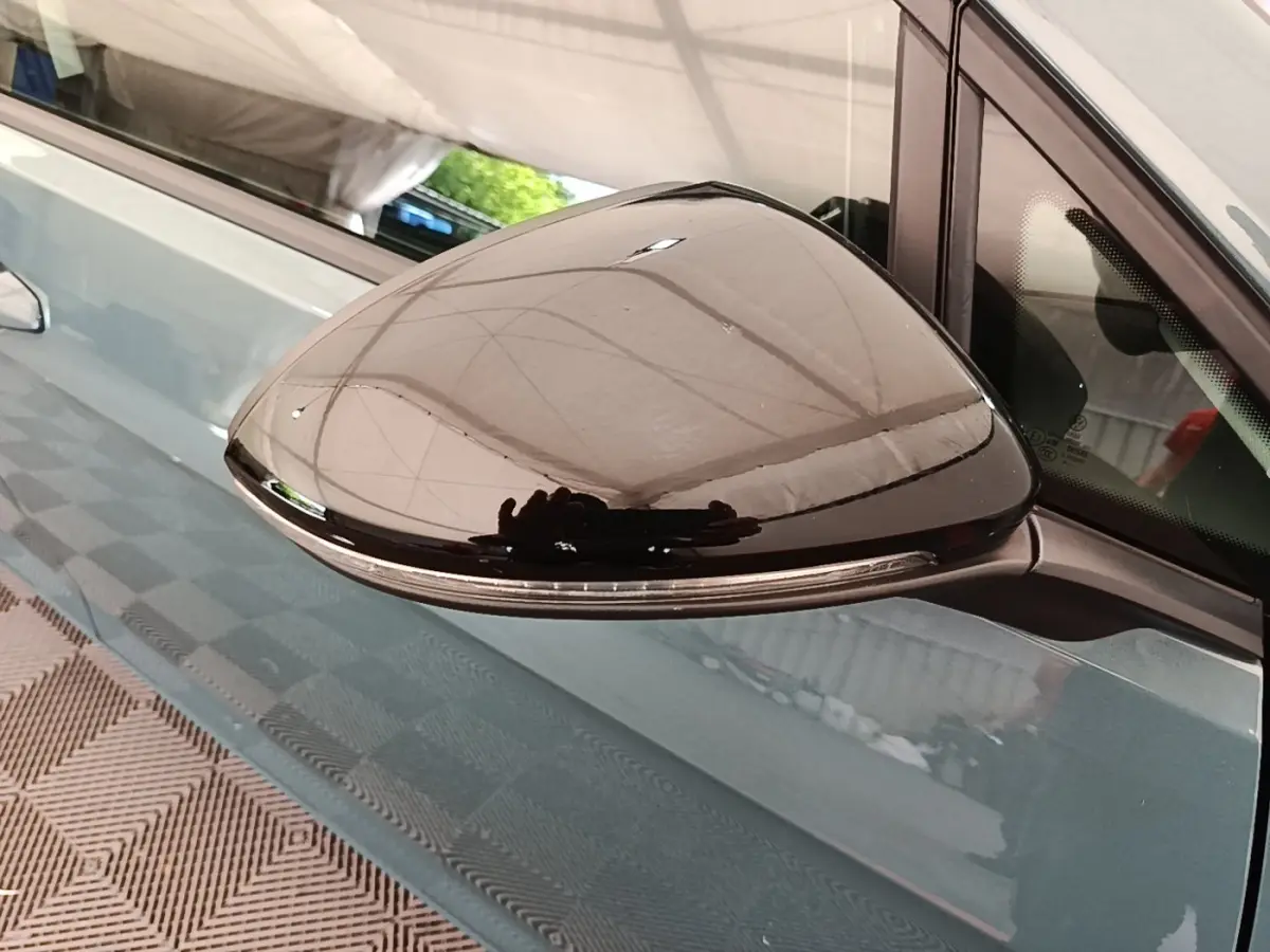 Rétroviseur extérieur noir en gros plan sur la porte côté gauche d’une Volkswagen Golf bleu clair.