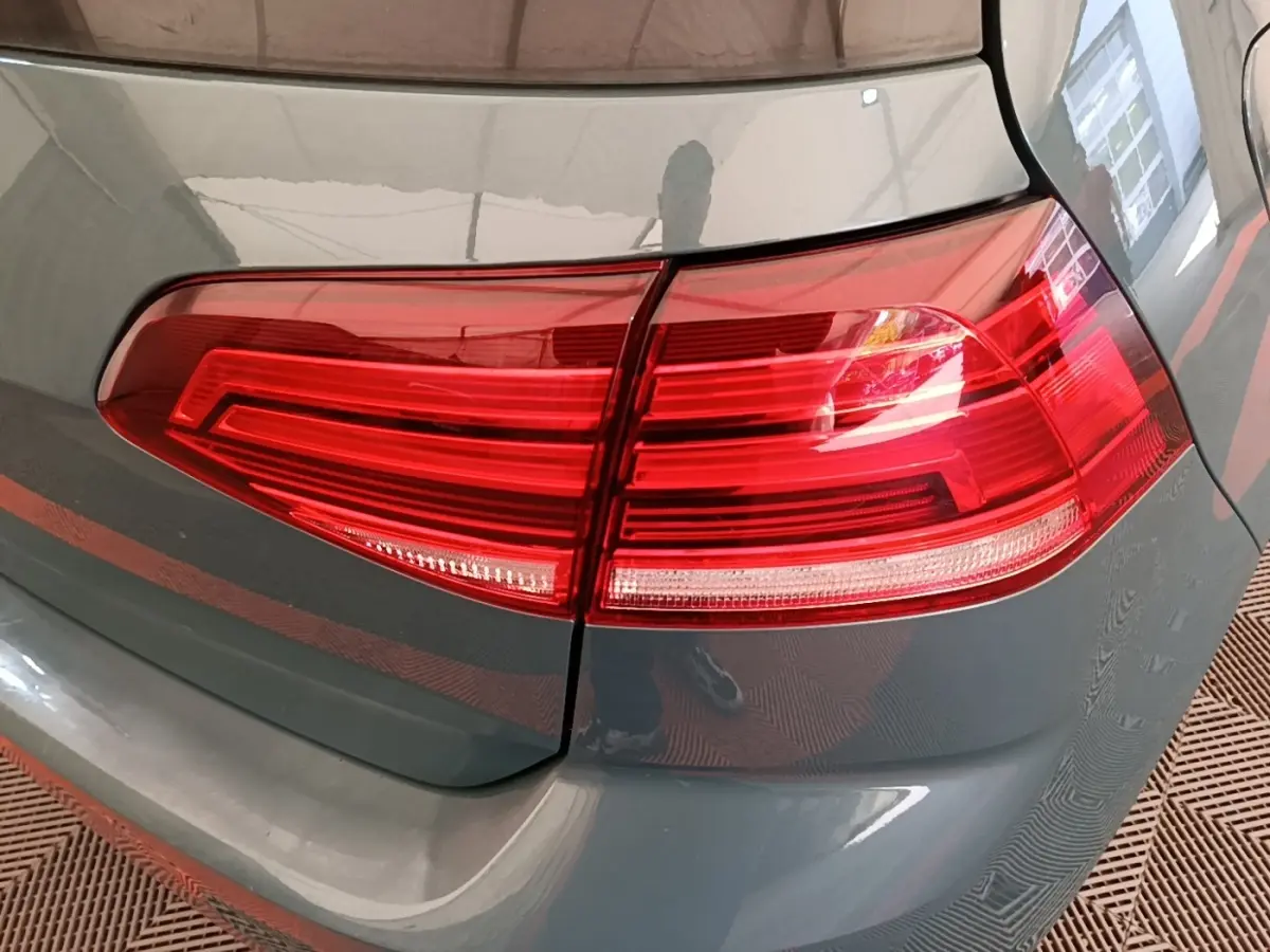 Gros plan sur le feu arrière droit rouge d’une Volkswagen Golf bleu foncé, avec reflet sur la carrosserie.