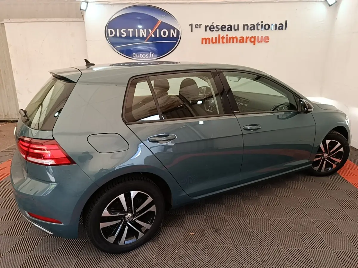 Vue 3/4 arrière droite d'une Volkswagen Golf bleu métallisé, avec jantes alliage et feux arrière LED allumés.
