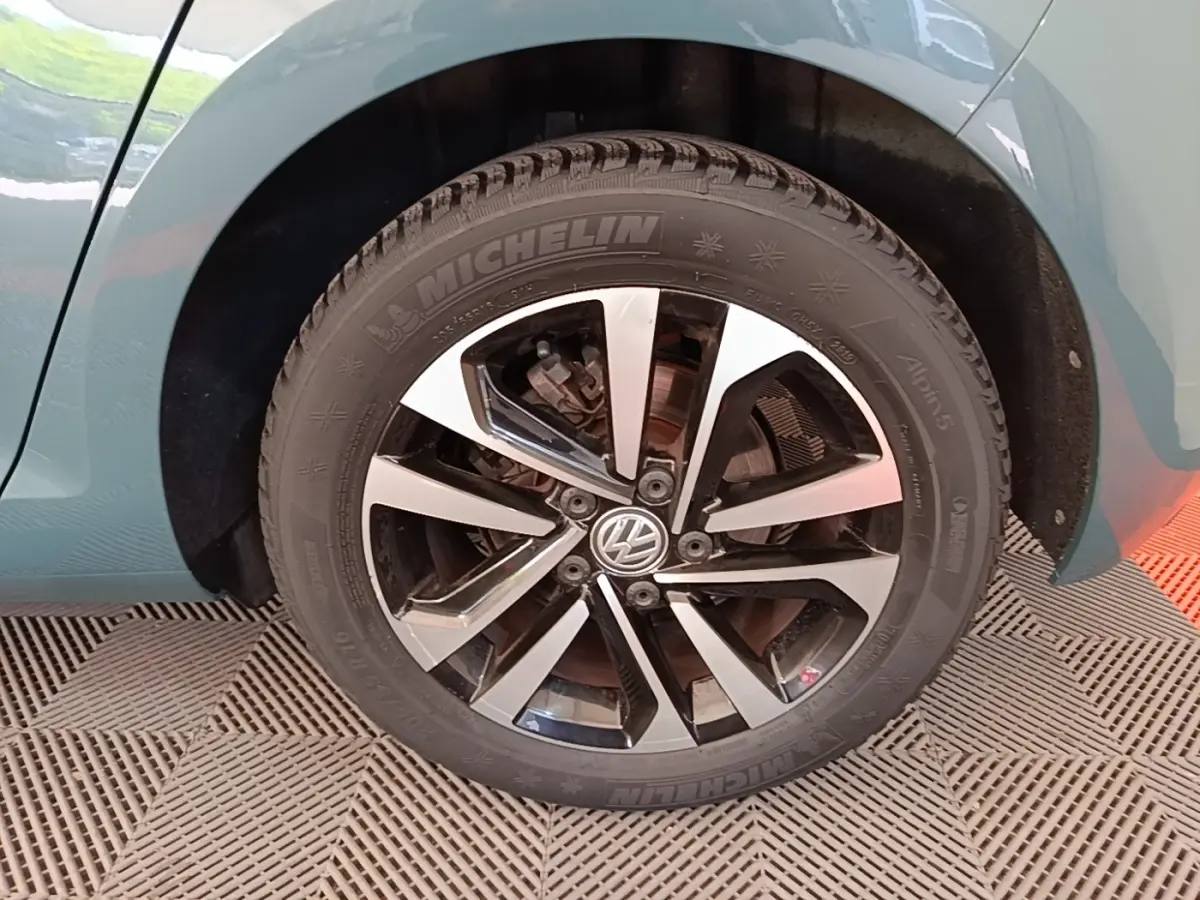 Gros plan sur la roue avant gauche d'une Volkswagen Golf bleue, jante alliage bicolore avec logo VW central.