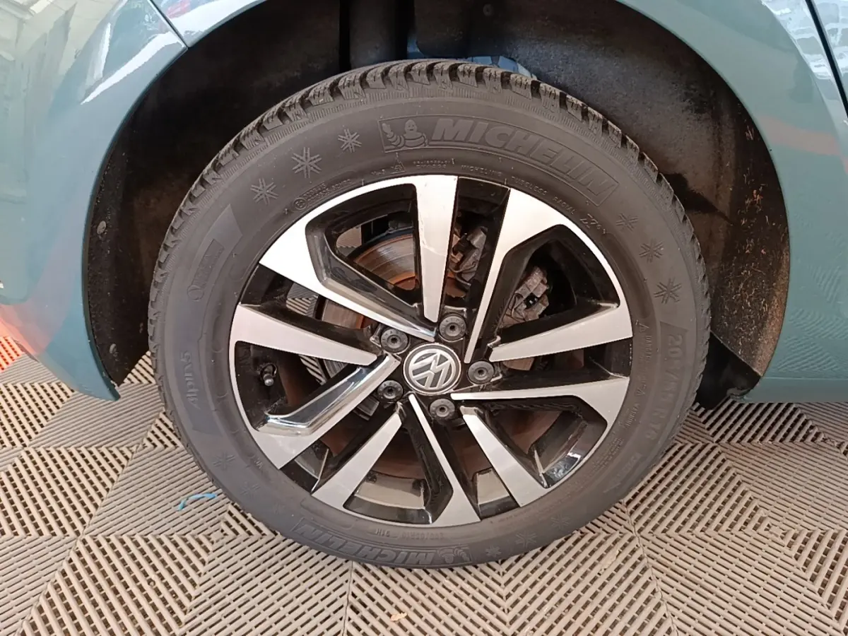 Gros plan sur la roue avant gauche d'une Volkswagen Golf bleue, mettant en valeur la jante alliage bicolore et le pneu hiver.