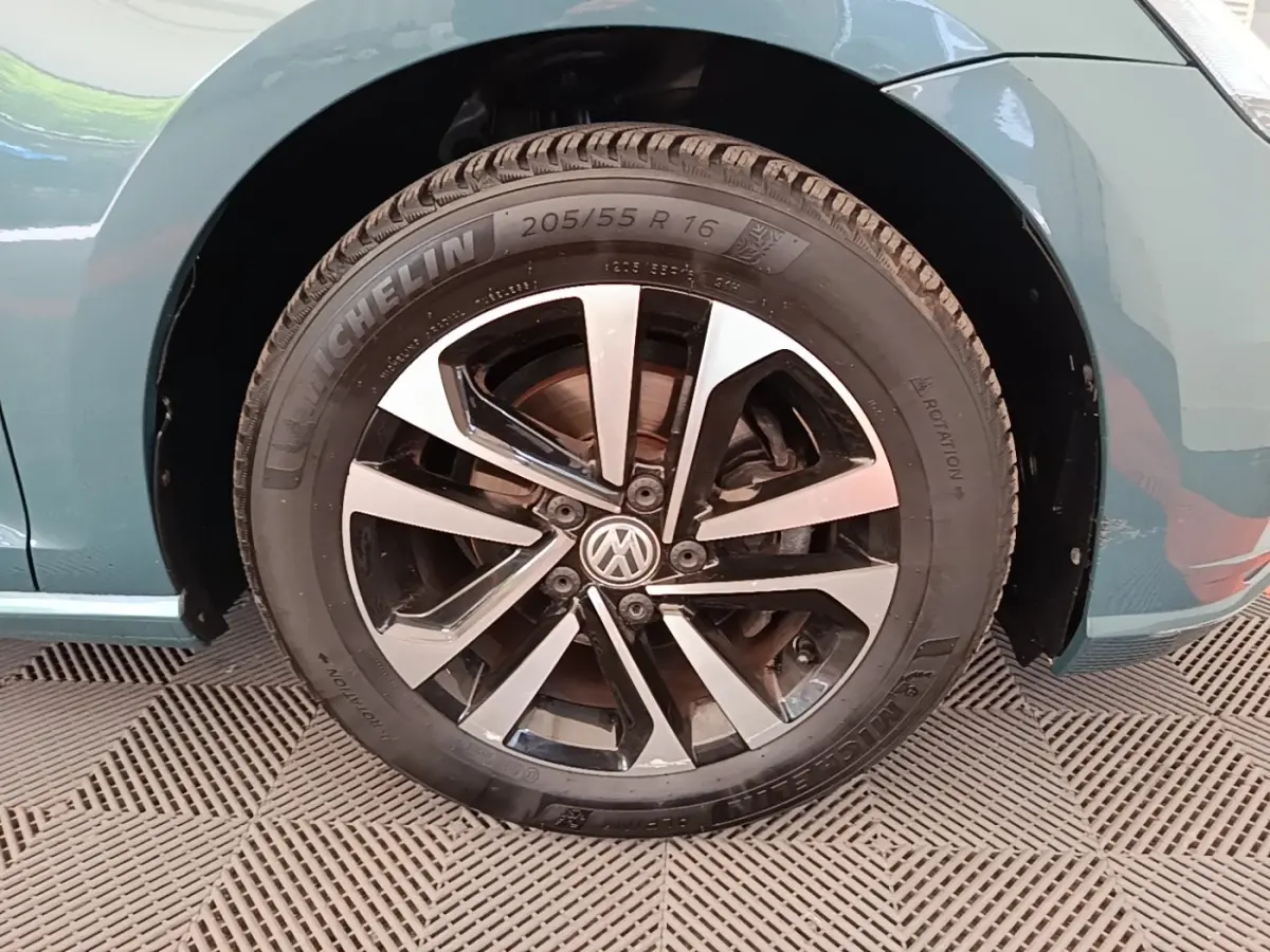 Gros plan sur la roue avant droite d'une Volkswagen Golf bleu, avec jante alliage bicolore et pneu Michelin.