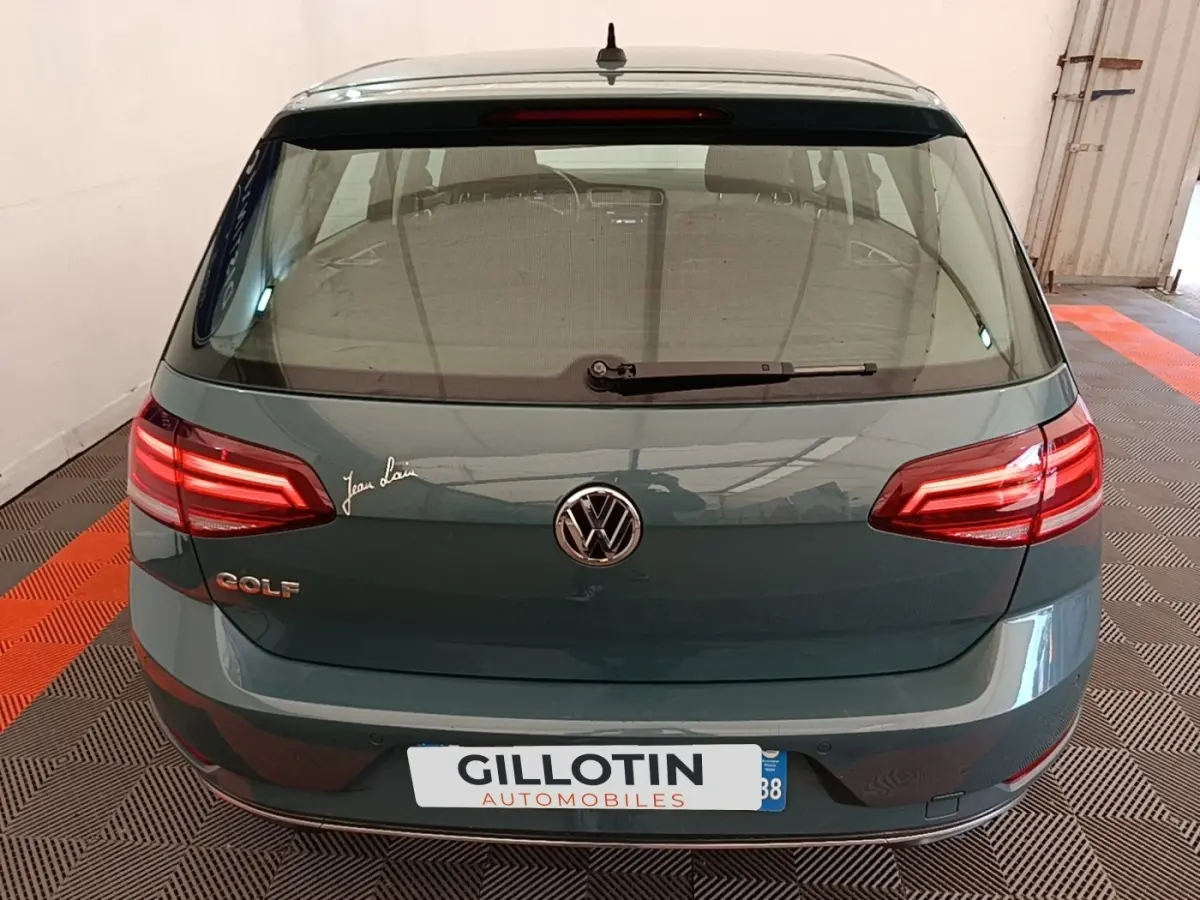 Vue arrière d'une Volkswagen Golf bleu foncé avec feux LED et logo VW visible dans un garage.