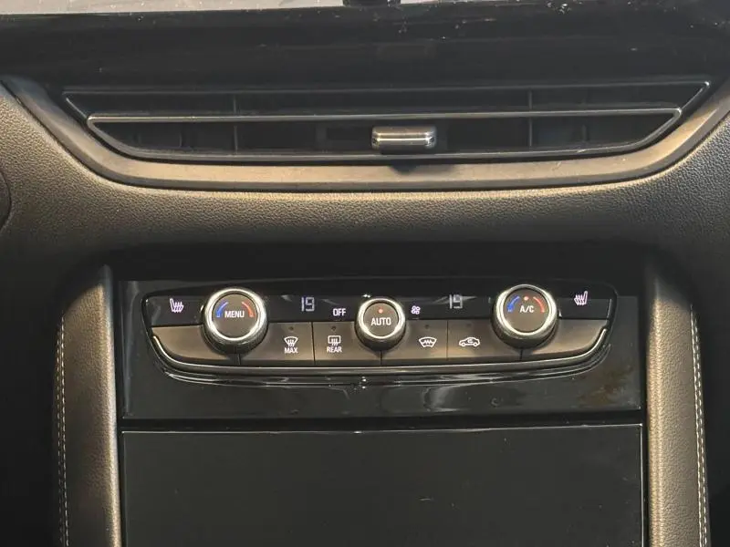 Gros plan sur la console centrale noire de l'Opel Grandland 2022, avec commandes climatisation bi-zone et sièges chauffants.