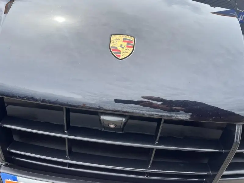 Gros plan sur la calandre avant noire d'une Porsche Macan 2018 avec l'écusson Porsche visible sur le capot.