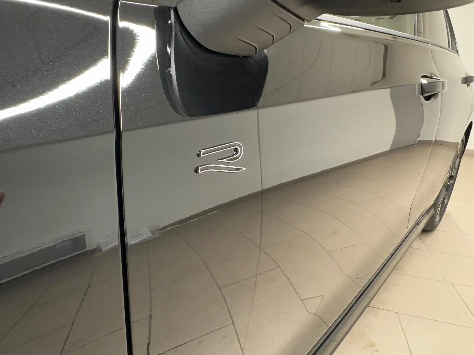 Gros plan sur la porte côté gauche noire grenadille d’une Volkswagen Golf 2.0 TDI R-Line avec logo R brillant.