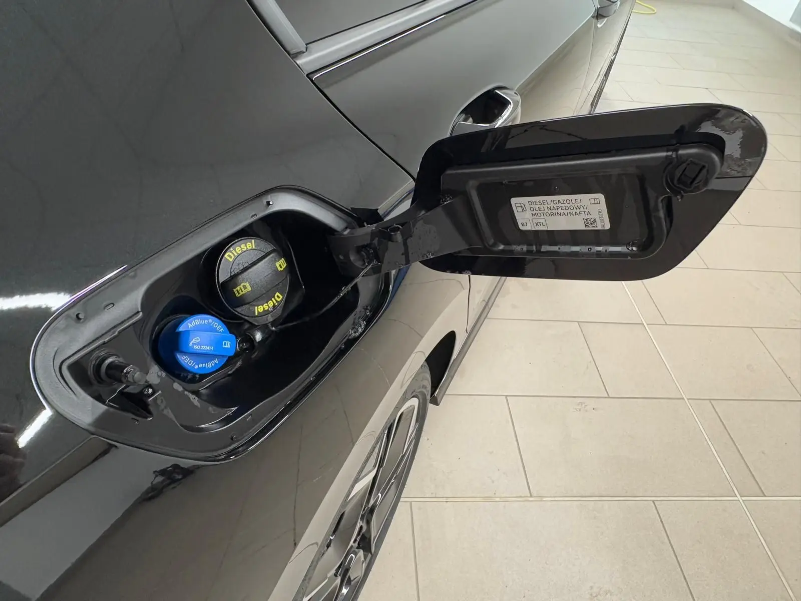 Vue rapprochée de la trappe à carburant ouverte côté gauche d'une Volkswagen Golf noire Grenadille avec bouchons Diesel et AdBlue visibles.