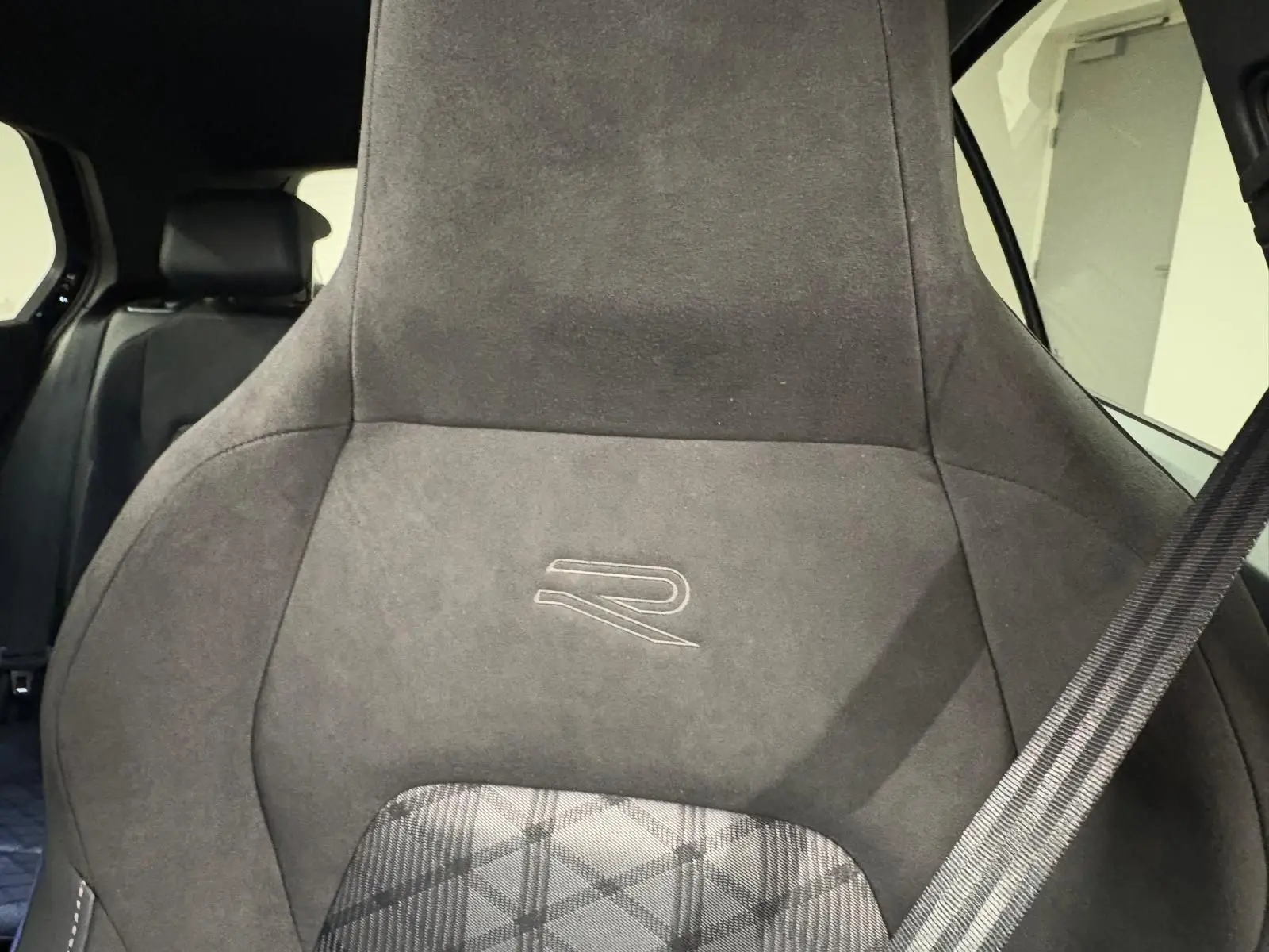 Gros plan sur le siège avant en alcantara gris foncé avec logo R, ceinture de sécurité visible à droite.