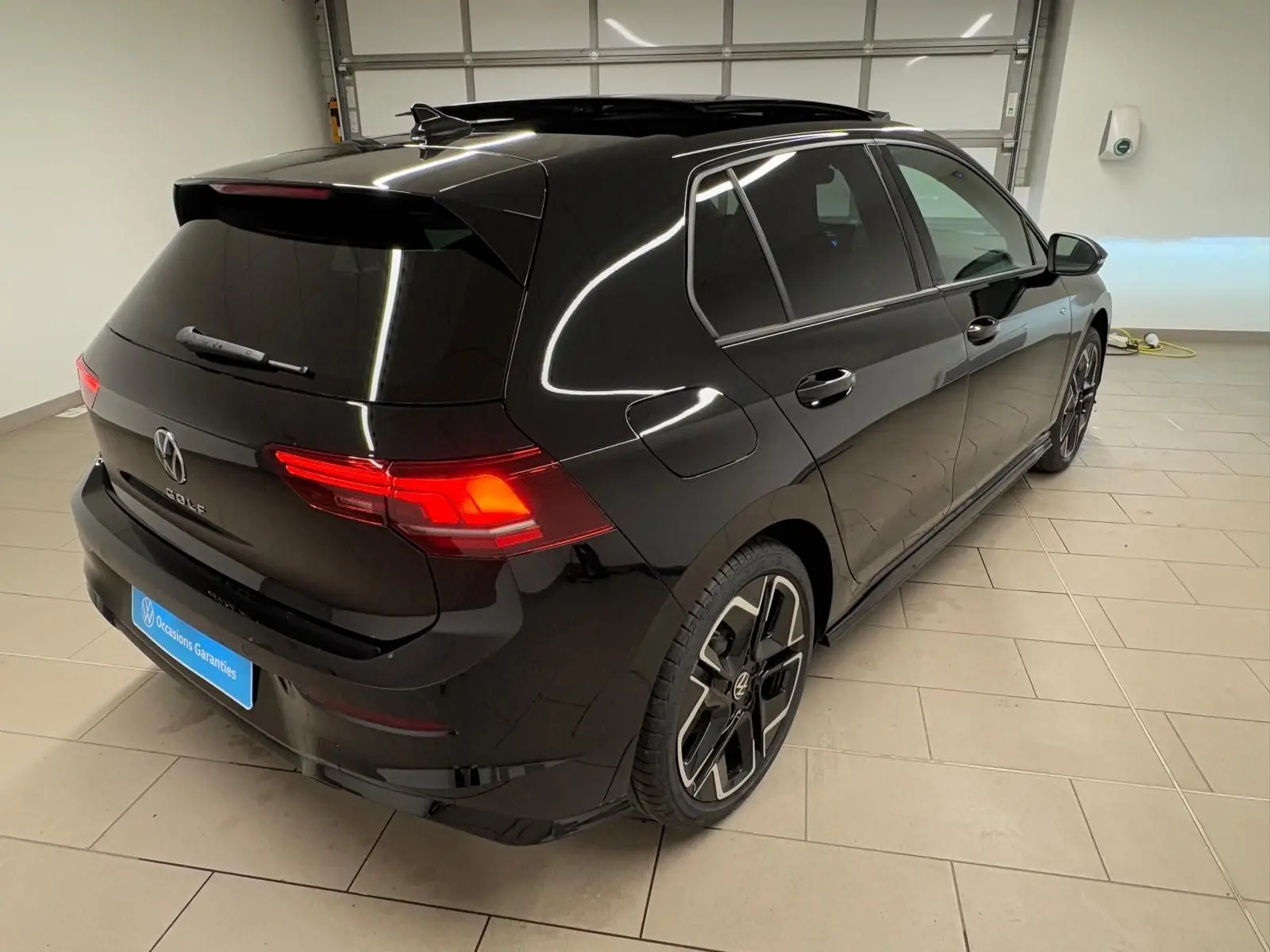 Vue 3/4 arrière droite d'une Volkswagen Golf 2.0 TDI noire Grenadille avec toit ouvrant panoramique en intérieur showroom.