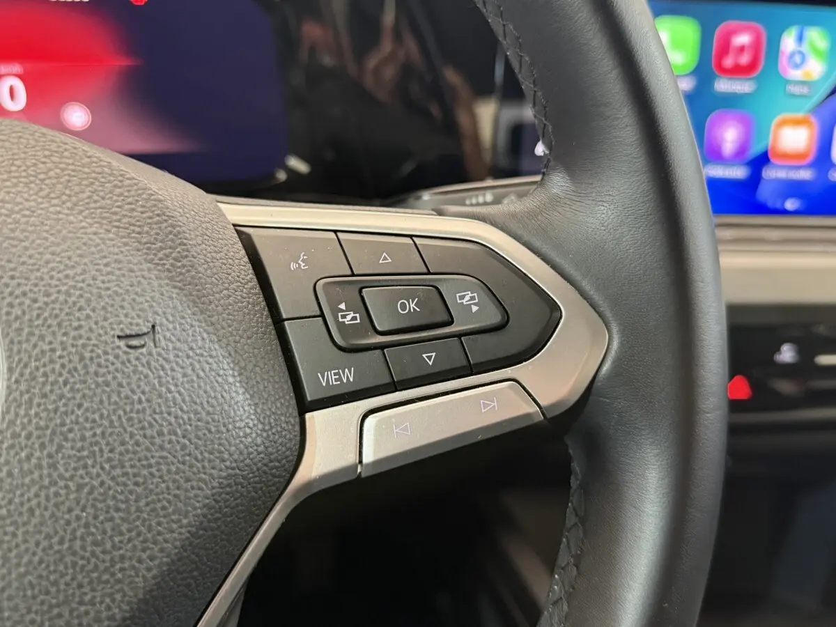 Gros plan sur le volant cuir noir de la Volkswagen Golf 2.0 TDI, avec commandes multifonctions et écran tactile en arrière-plan.