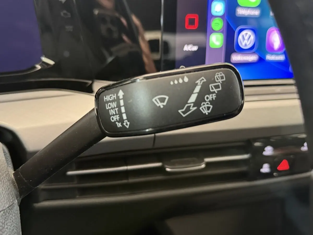 Gros plan sur la commande des essuie-glaces dans l’habitacle d’une Volkswagen Golf bleu, avec écran tactile en arrière-plan.