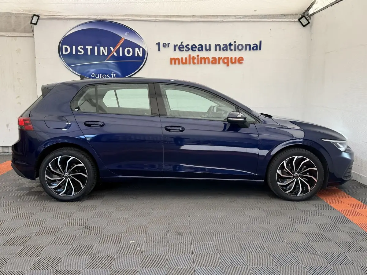 Profil droit d'une Volkswagen Golf bleu foncé 2021 avec jantes alliage noires et détails argentés, en intérieur showroom.