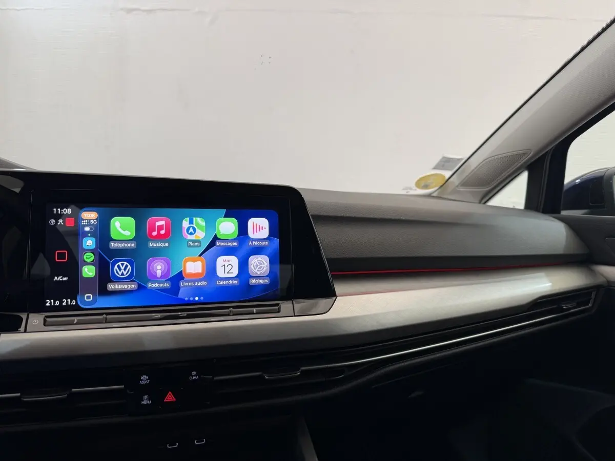 Vue intérieure côté passager du tableau de bord de la Volkswagen Golf bleu, avec écran tactile et bandeau lumineux rouge.