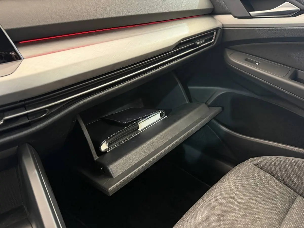 Intérieur Volkswagen Golf 2.0 TDI 2021, vue sur boîte à gants ouverte avec livret, tableau de bord noir et garniture claire.