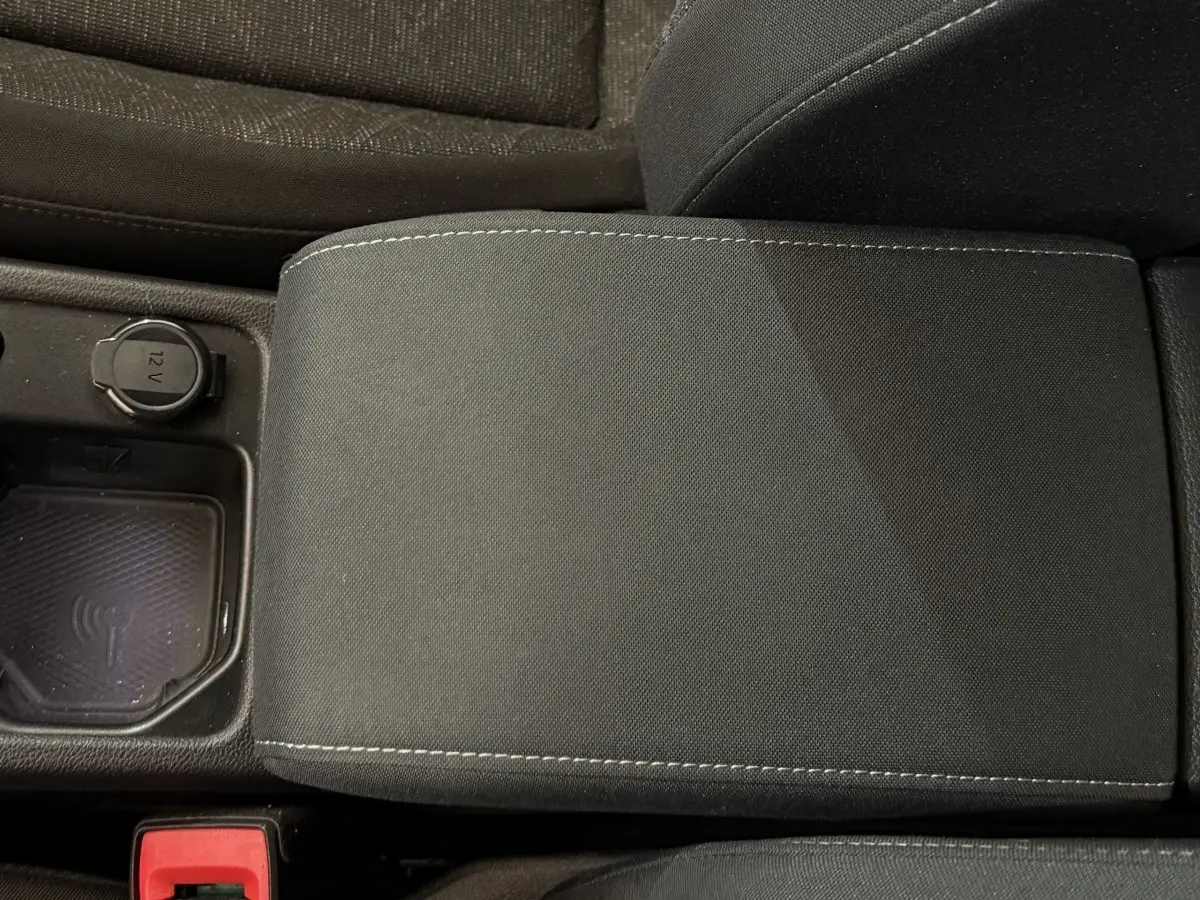 Gros plan sur l'accoudoir central noir et la prise 12V avec zone de recharge à induction dans une Volkswagen Golf bleue.