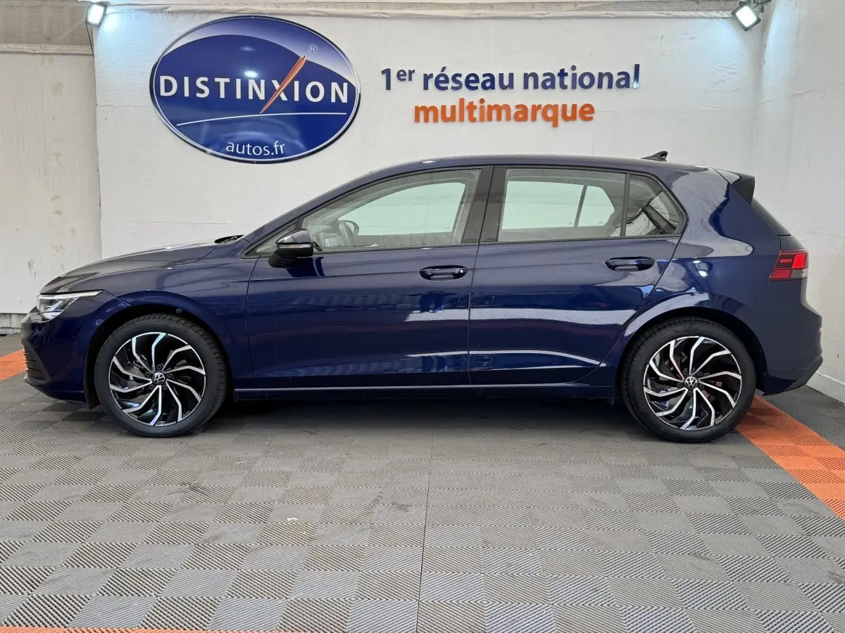 Profil côté gauche d'une Volkswagen Golf 2.0 TDI bleu foncé avec jantes alliage noires et argentées, en intérieur showroom.