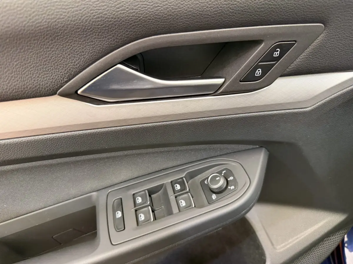 Gros plan sur la porte côté conducteur de la Volkswagen Golf bleu, montrant les commandes des vitres et le bouton de verrouillage.