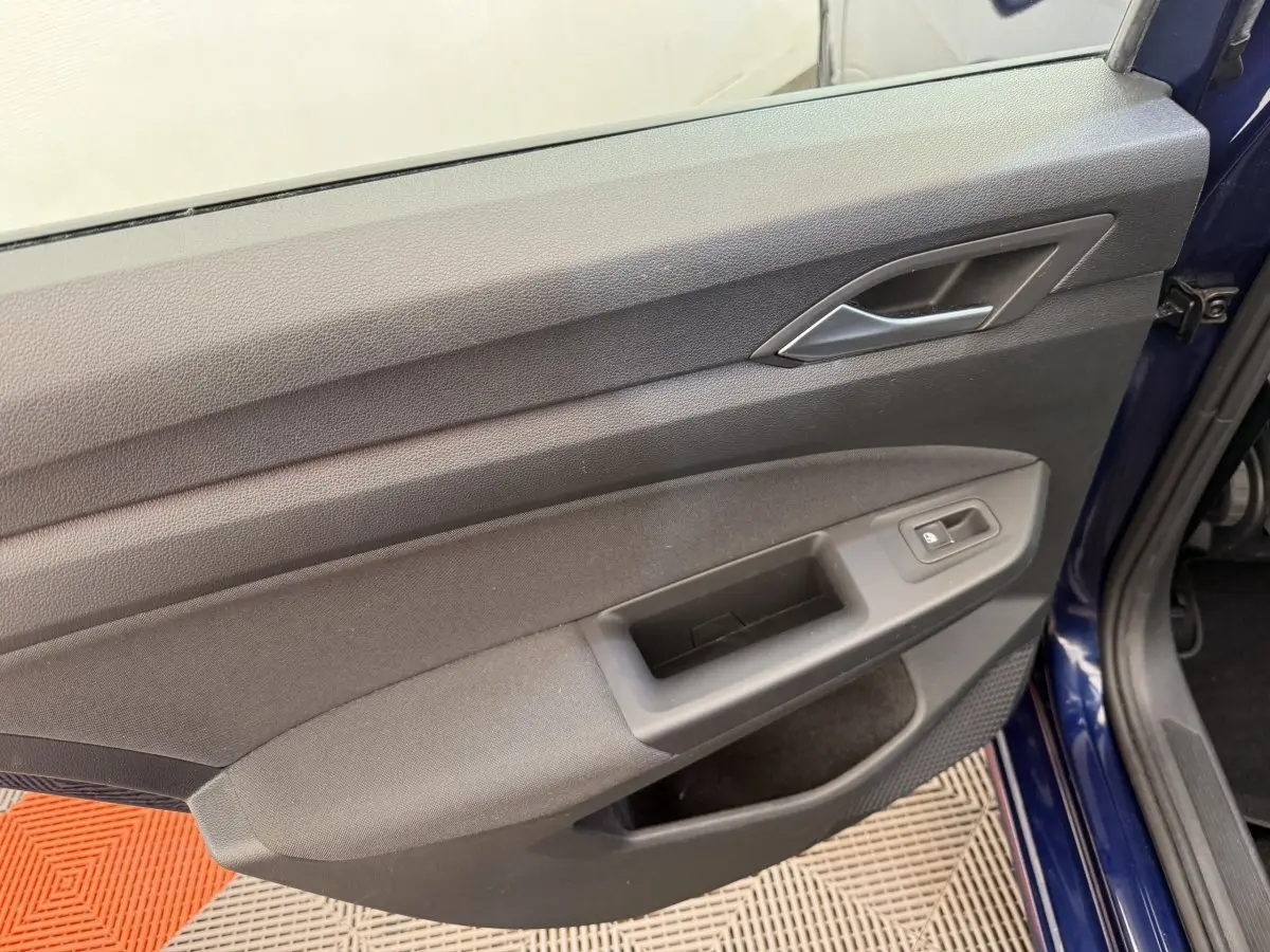 Vue rapprochée de la porte avant gauche bleu foncé d'une Volkswagen Golf 2021, avec poignée intérieure grise.