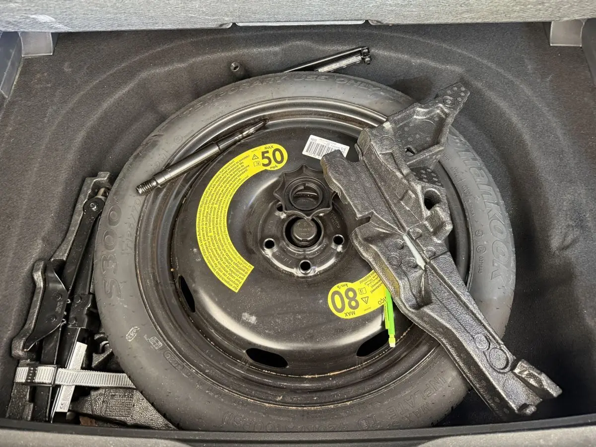 Vue rapprochée de la roue de secours noire et des outils dans le coffre d’une Volkswagen Golf bleu 2021.
