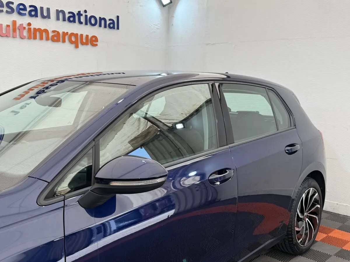 Vue côté gauche d'une Volkswagen Golf bleu métallisé 5 portes avec rétroviseur noir et jantes alliage distinctives.
