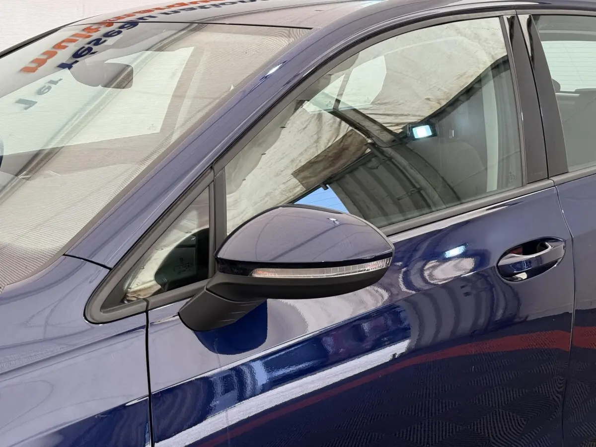 Vue rapprochée du côté gauche d'une Volkswagen Golf bleu métallisé, mettant en valeur le rétroviseur et la poignée de porte.