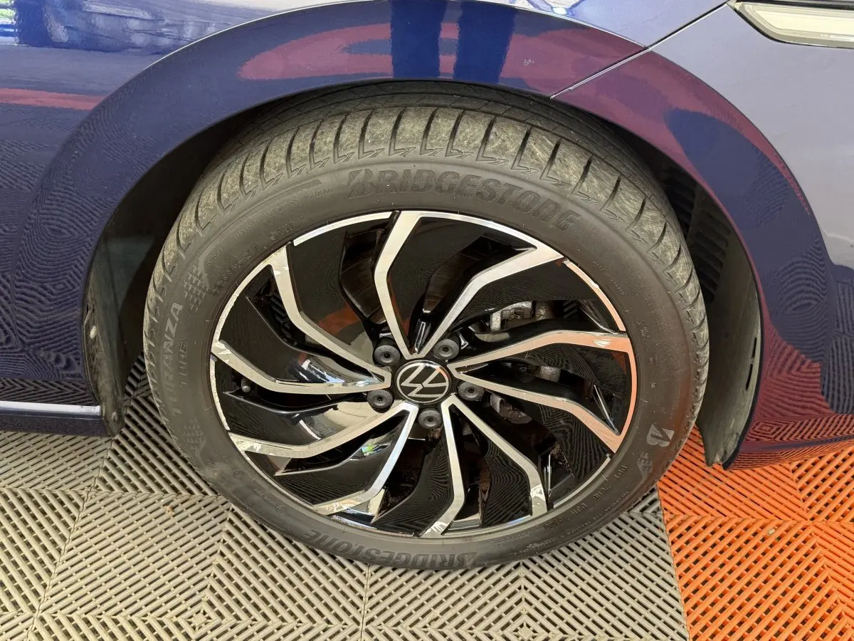 Gros plan sur la roue avant droite d’une Volkswagen Golf bleu, jante alliage noir et argentée au design dynamique.
