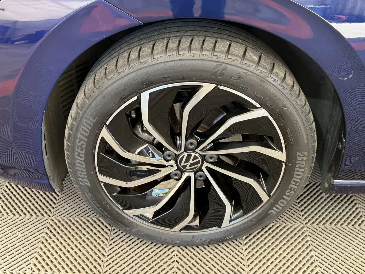 Gros plan sur la roue avant droite d’une Volkswagen Golf bleu 2021 avec jante noire et argentée au design moderne.