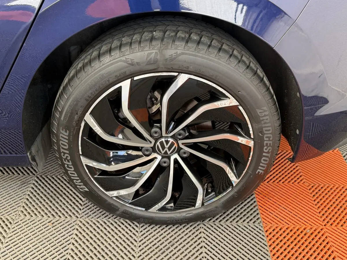 Gros plan sur la roue avant droite d'une Volkswagen Golf bleue, avec jante alliage noire et chromée distinctive.