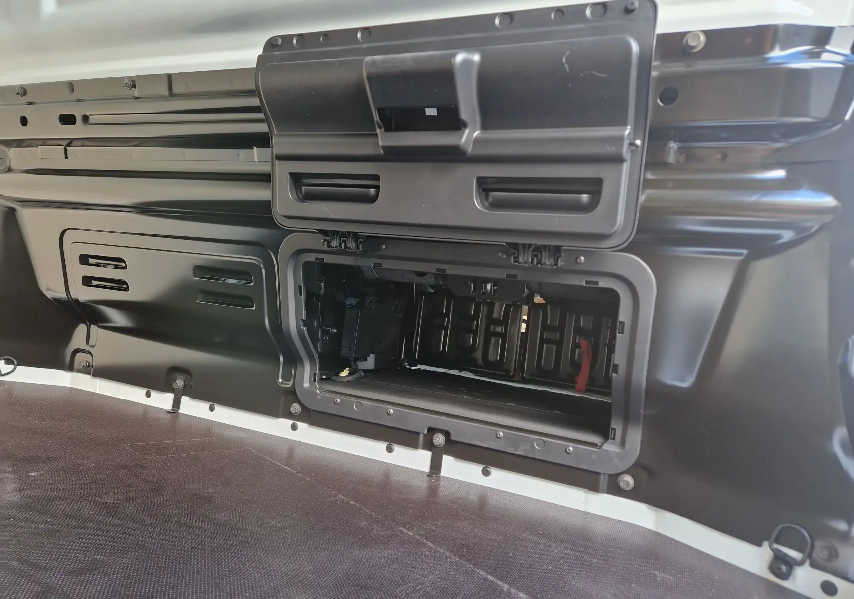 Vue intérieure du compartiment de chargement du Nissan Primastar blanc 2025, avec trappe de rangement ouverte côté gauche.