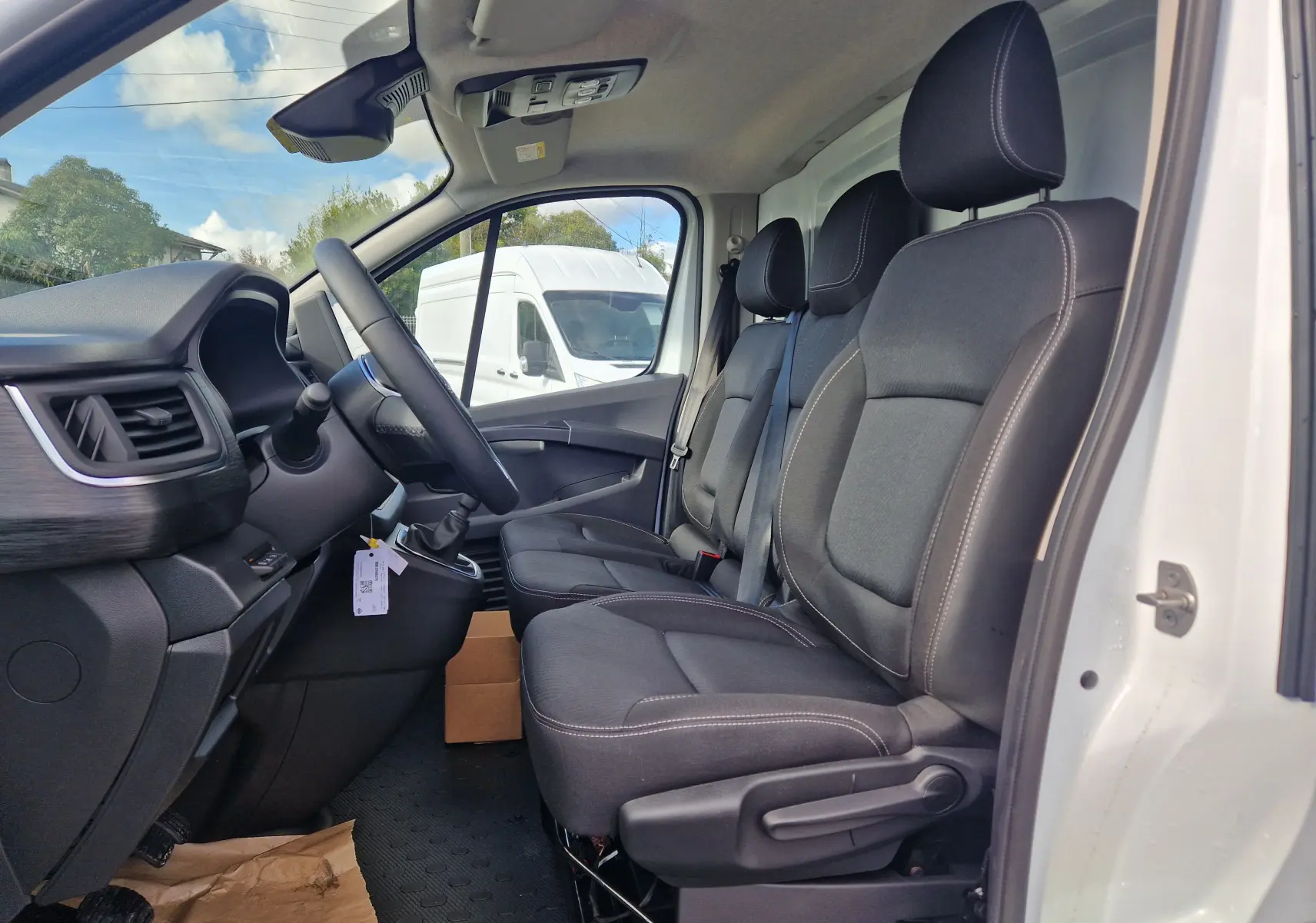 Vue intérieure côté conducteur du Nissan Primastar blanc 2025, montrant les sièges noirs et le tableau de bord avec volant.