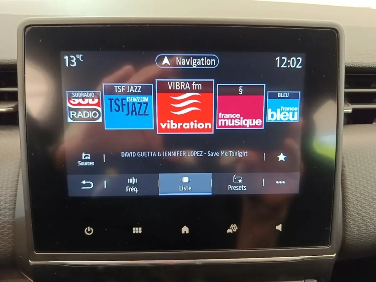 Écran tactile central de la Renault Clio Intens gris foncé, affichant les radios et la navigation à 12h02.