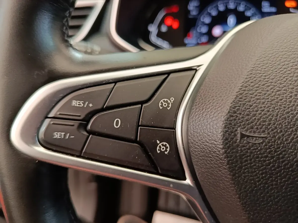 Gros plan sur les commandes de régulateur de vitesse au volant cuir noir de la Renault Clio Intens TCe 100 gris foncé 2020.