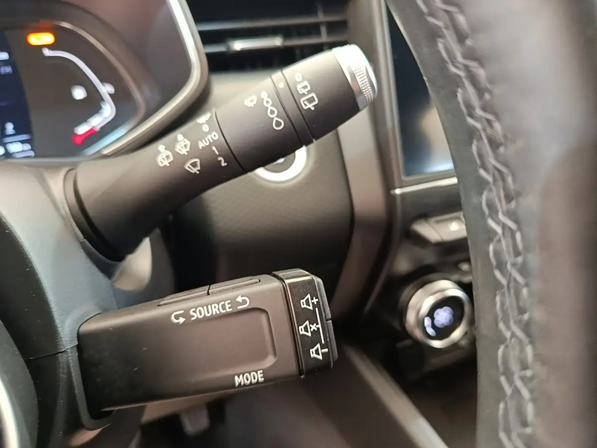 Gros plan sur les commandes au volant d’une Renault Clio Intens gris foncé, avec tableau de bord et bouton démarrage visibles.
