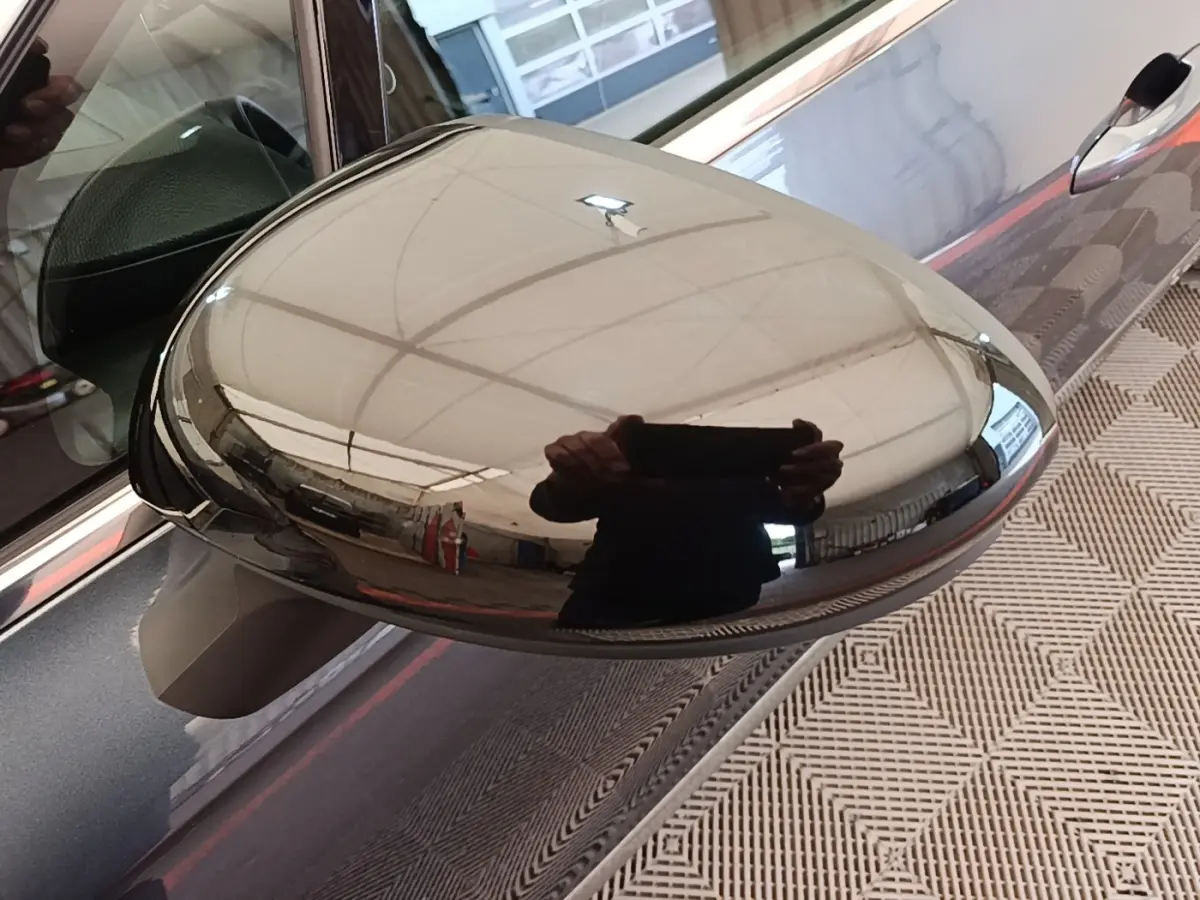 Rétroviseur droit chromé reflétant l'intérieur d'un garage sur une Renault Clio gris foncé vue de côté.