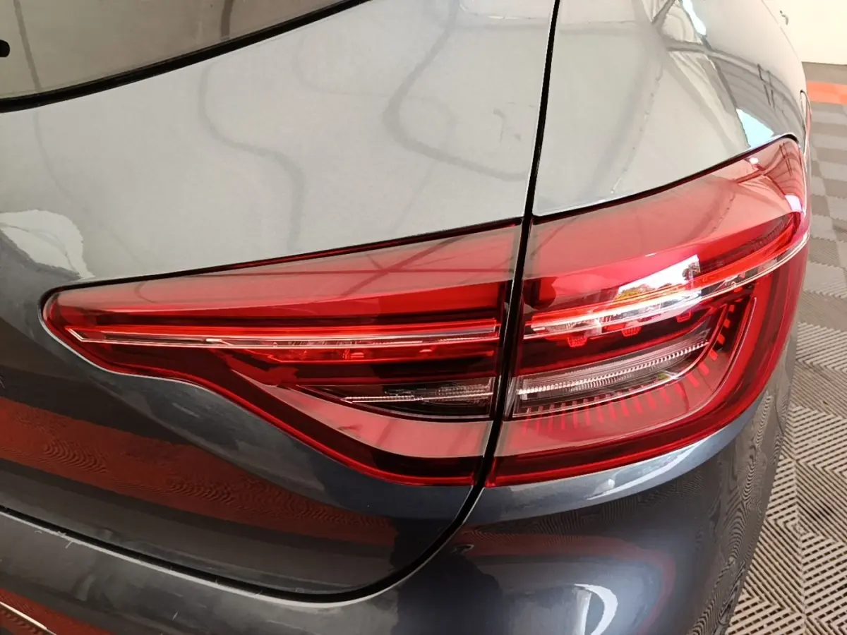 Gros plan sur le feu arrière droit rouge d'une Renault Clio Intens gris foncé, avec partie de la carrosserie visible.