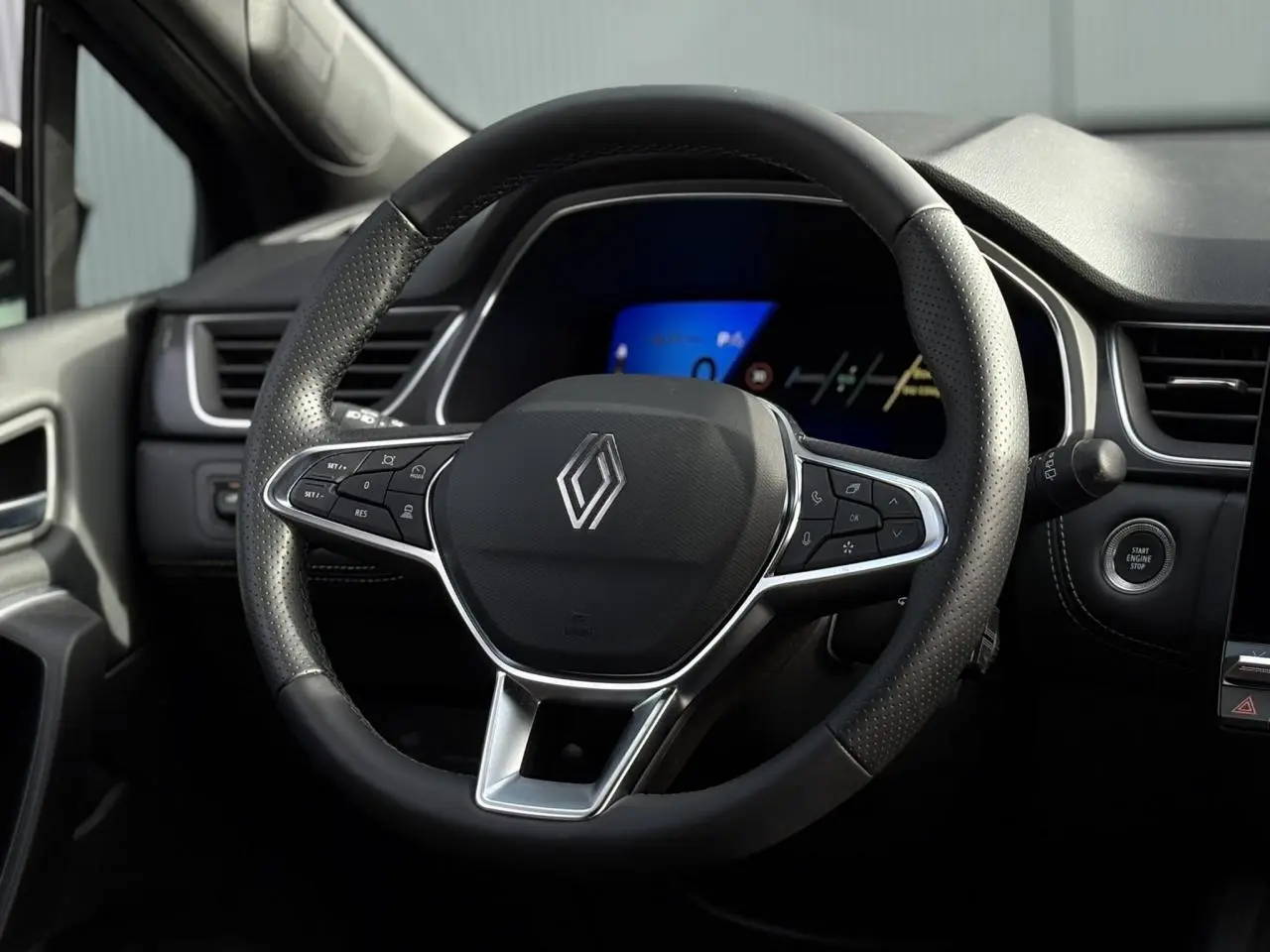 Vue rapprochée du volant noir perforé de la Renault SYMBIOZ 2025 avec tableau de bord numérique bleu en arrière-plan.