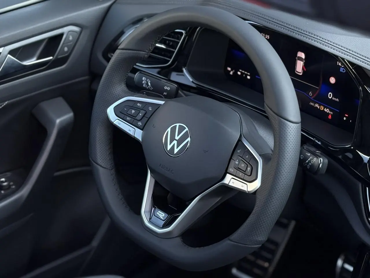 Gros plan sur le volant cuir noir avec logo VW et combiné digital du tableau de bord du Volkswagen T-Roc R-Line.