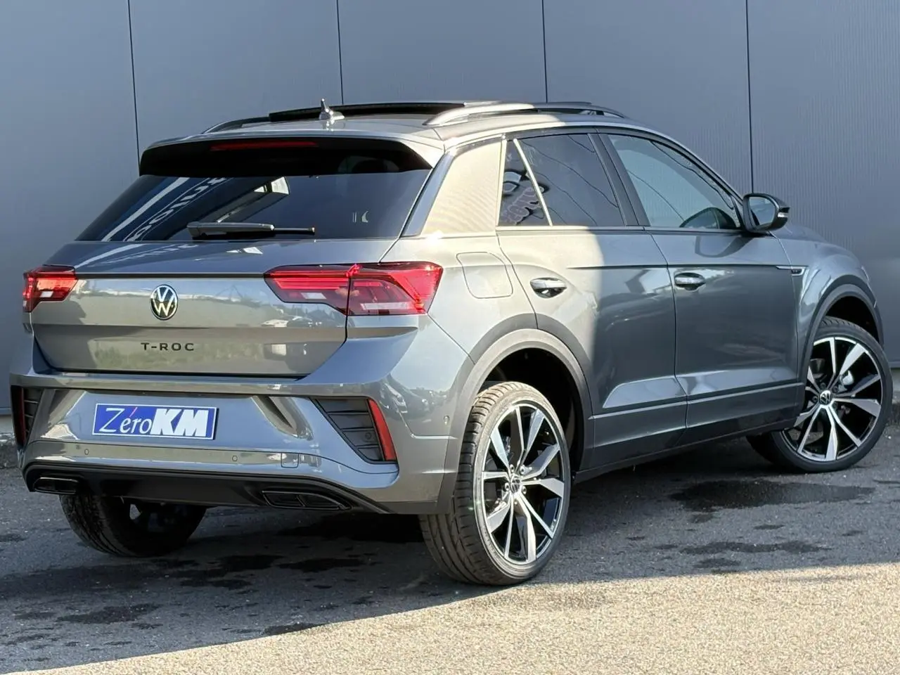 Volkswagen T-Roc gris Indium en 3/4 arrière droit avec jantes alliage 19 pouces et toit ouvrant visible.