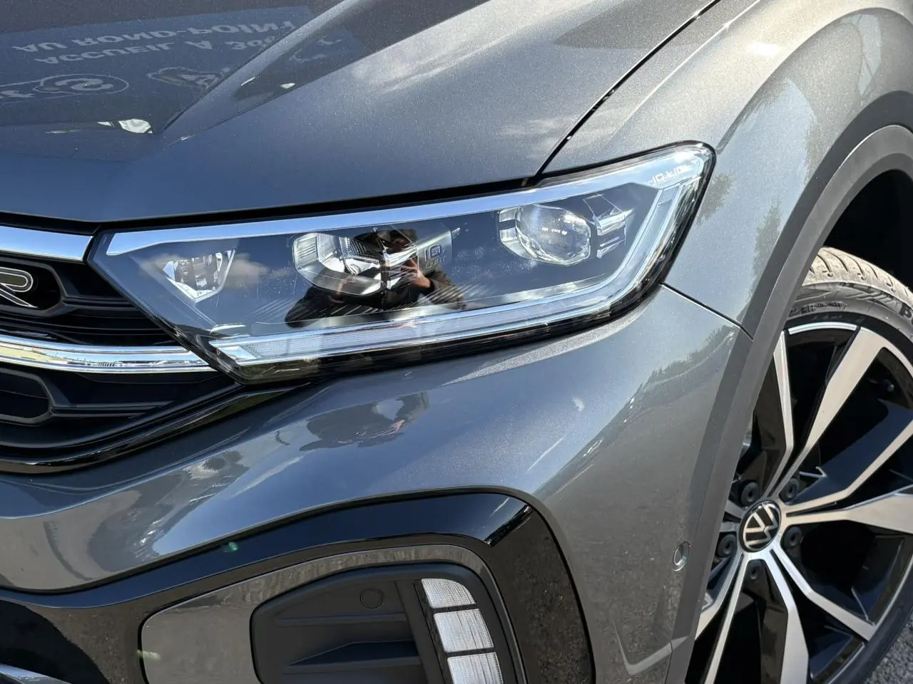 Gros plan sur l'avant droit du Volkswagen T-Roc gris Indium, mettant en valeur le phare LED et la jante alliage R-Line.
