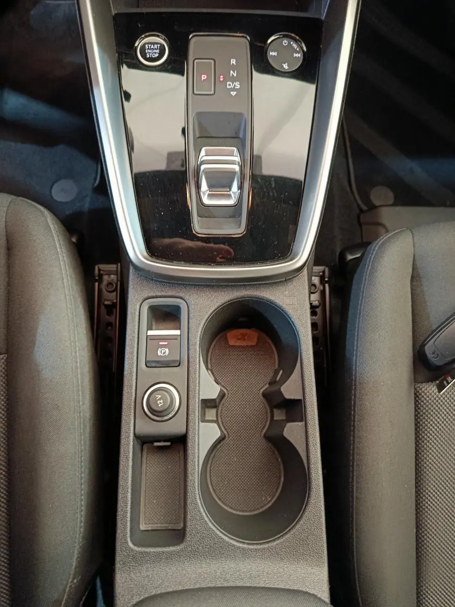 Vue plongeante sur la console centrale noire de l'Audi A3 30 TFSI MHEV avec boîte auto et porte-gobelets intégrés.