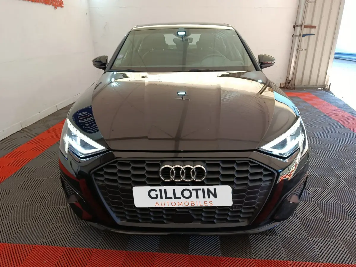 Vue frontale d'une Audi A3 noire 2022 avec calandre hexagonale et phares LED allumés dans un showroom.