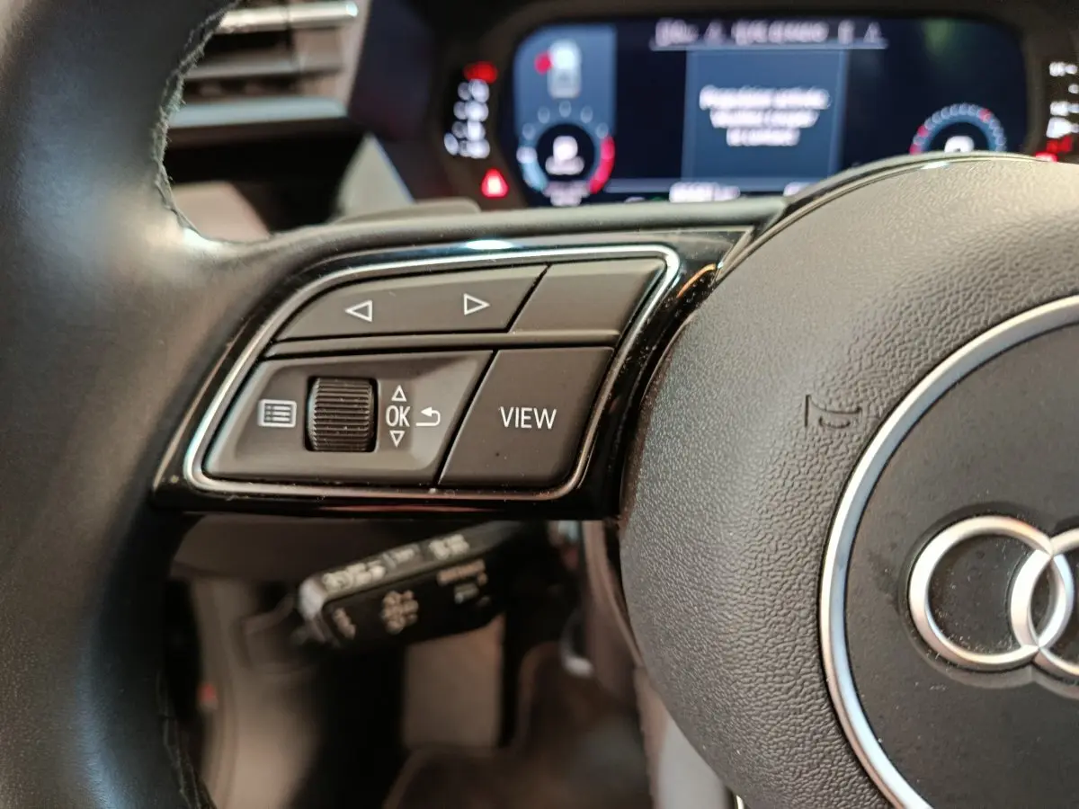 Gros plan sur le volant cuir noir de l'Audi A3 2022 avec commandes multifonctions et combiné d'instruments numérique.