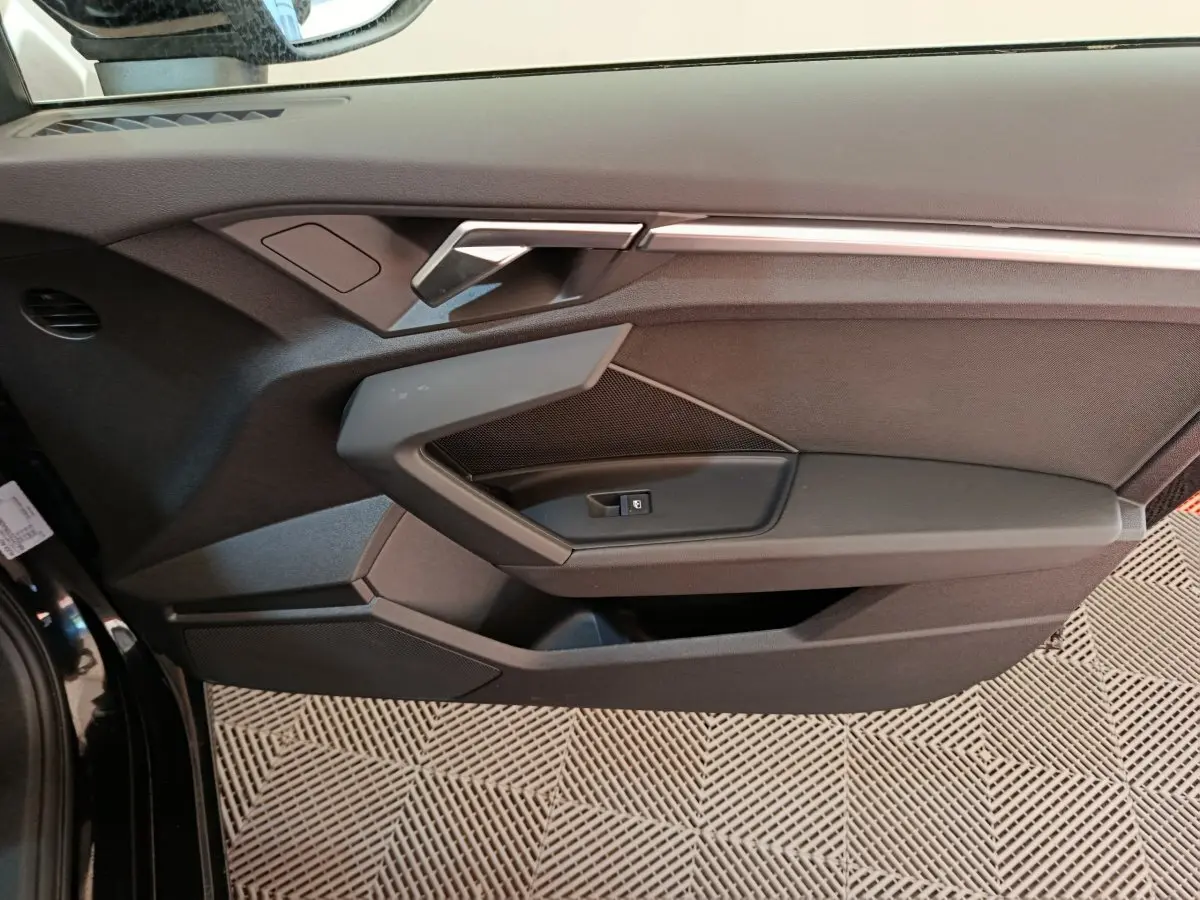 Vue rapprochée de la porte avant gauche noire de l'Audi A3 30 TFSI MHEV avec poignée et commande de fenêtre intégrées.